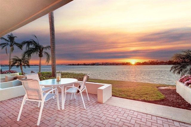 patio terrace at dusk featuring outdoor dining area and a water view