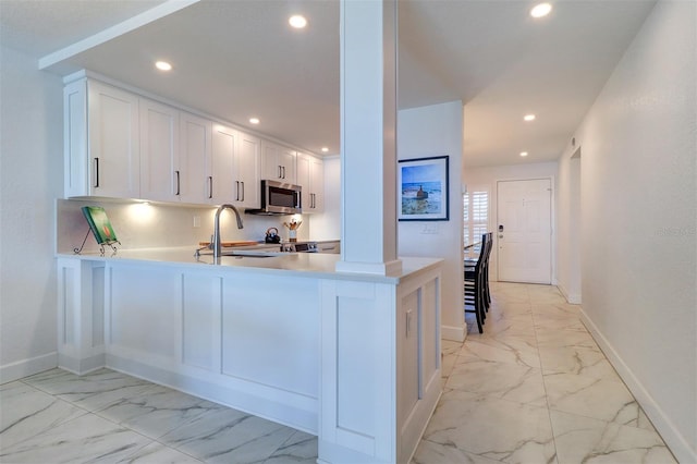 kitchen with a sink, white cabinets, marble finish floor, light countertops, and stainless steel microwave