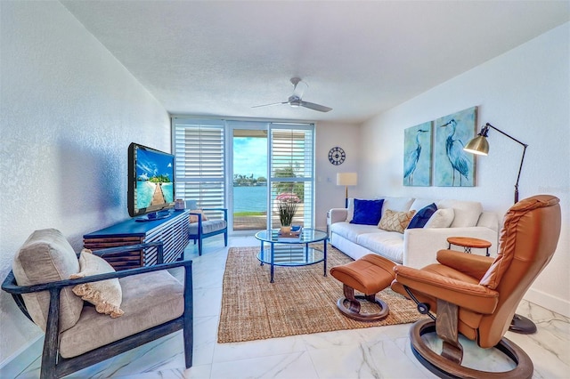 living area featuring a ceiling fan, marble finish floor, a textured wall, and baseboards