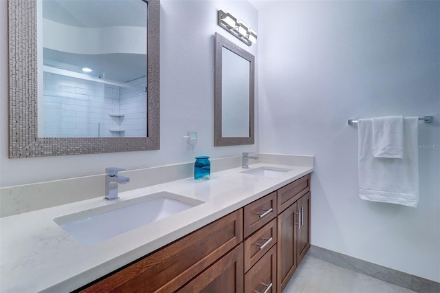 full bath with double vanity, baseboards, a tile shower, and a sink