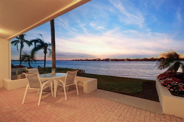 patio terrace at dusk with outdoor dining area and a water view