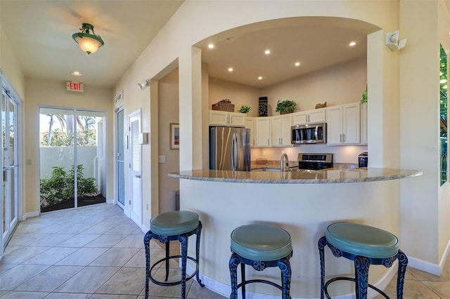 kitchen with stainless steel appliances, a breakfast bar, a peninsula, white cabinets, and light stone countertops