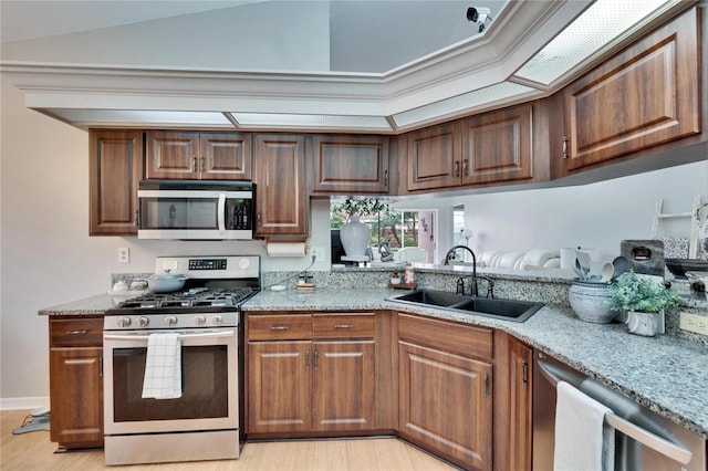 kitchen featuring light wood-style flooring, appliances with stainless steel finishes, light stone counters, vaulted ceiling, and a sink