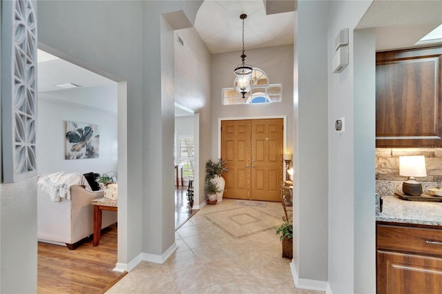 foyer entrance with light tile patterned flooring, a towering ceiling, visible vents, baseboards, and an inviting chandelier