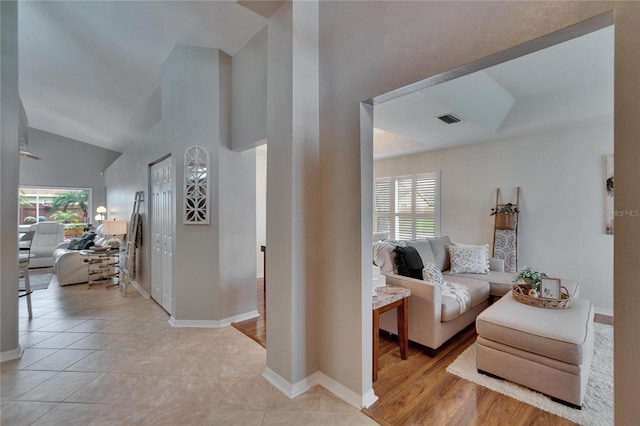 hallway featuring light tile patterned floors, high vaulted ceiling, visible vents, and baseboards