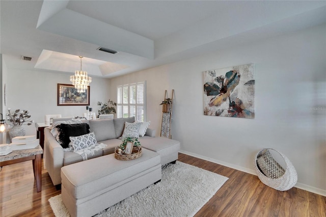 living area with baseboards, visible vents, a tray ceiling, and wood finished floors