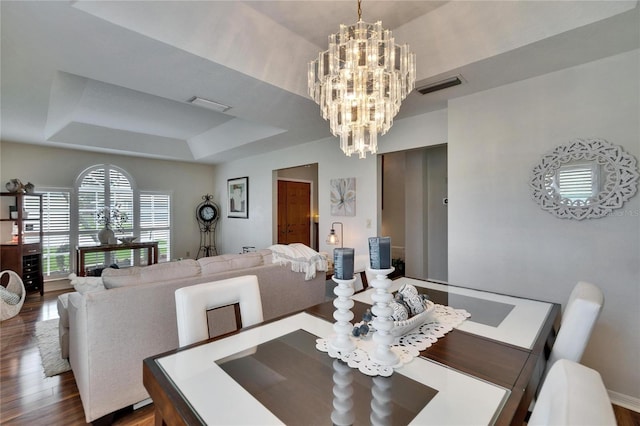 dining area featuring a tray ceiling, dark wood-style flooring, visible vents, and a notable chandelier