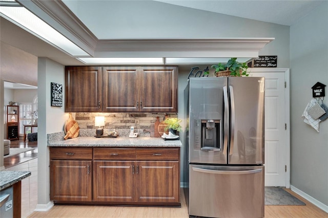 kitchen featuring light wood-style floors, decorative backsplash, light stone counters, and stainless steel fridge with ice dispenser