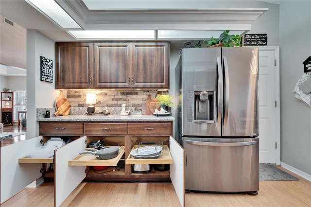 kitchen featuring light stone counters, visible vents, light wood-type flooring, stainless steel fridge with ice dispenser, and tasteful backsplash