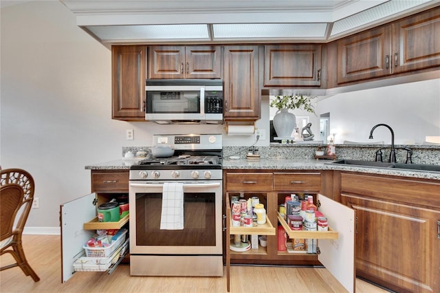 kitchen with light wood finished floors, appliances with stainless steel finishes, light stone counters, and a sink