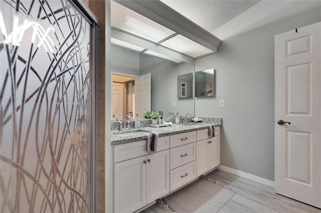 bathroom with a textured ceiling, double vanity, a sink, and wood finished floors