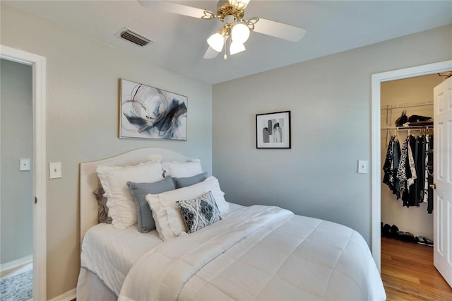 bedroom featuring a walk in closet, a closet, visible vents, a ceiling fan, and wood finished floors