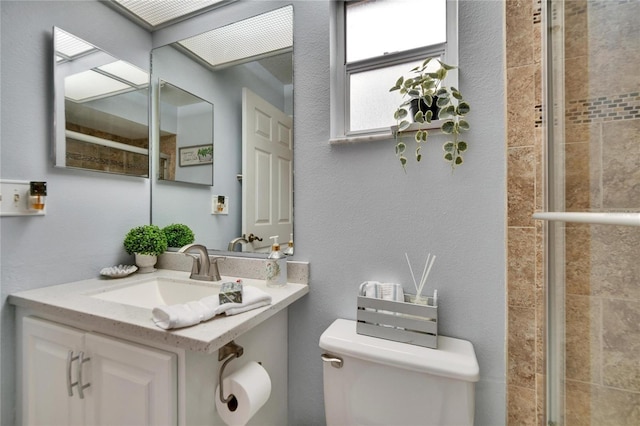 bathroom featuring toilet, vanity, tiled shower, and a textured wall