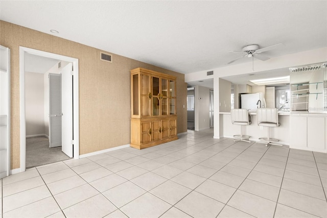 unfurnished living room with light tile patterned floors, ceiling fan, visible vents, and baseboards