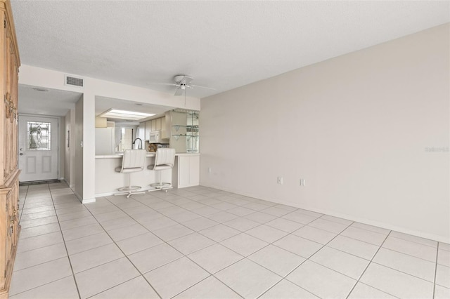unfurnished living room featuring ceiling fan, light tile patterned floors, a textured ceiling, visible vents, and baseboards