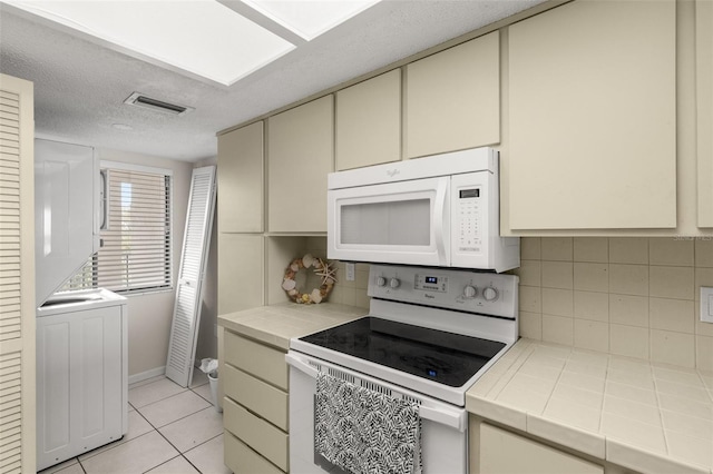 kitchen with cream cabinetry, tile counters, visible vents, backsplash, and white appliances