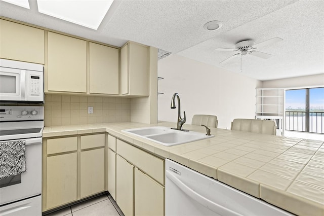 kitchen featuring tasteful backsplash, cream cabinets, a sink, white appliances, and a peninsula
