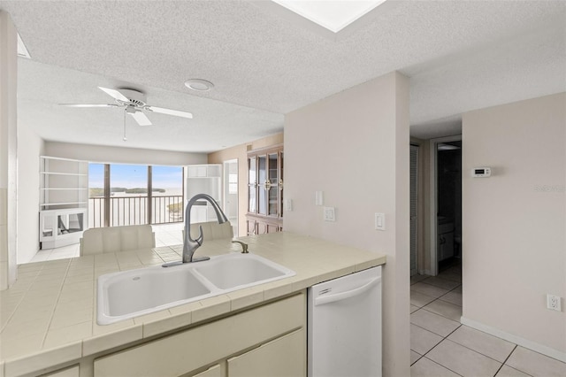 kitchen with light tile patterned floors, dishwasher, tile countertops, a textured ceiling, and a sink