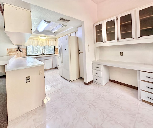 kitchen featuring white refrigerator with ice dispenser, light countertops, visible vents, built in study area, and a peninsula