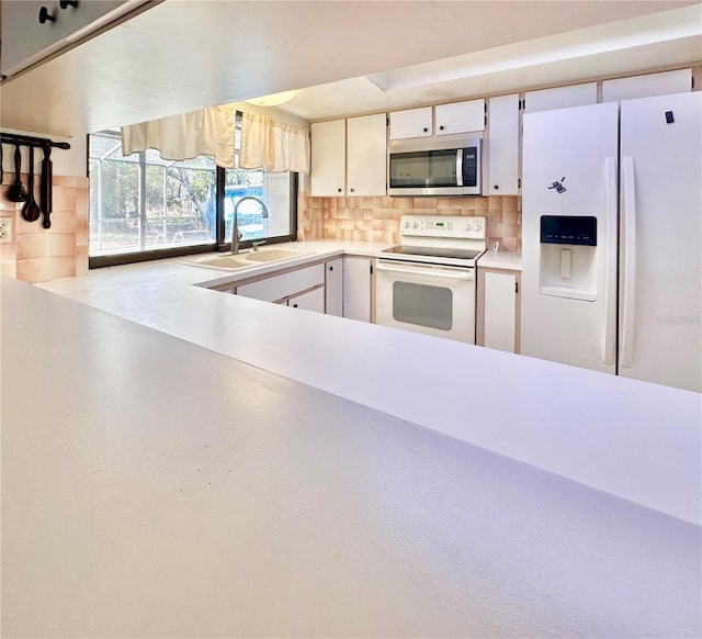 kitchen with white appliances, tasteful backsplash, light countertops, white cabinetry, and a sink