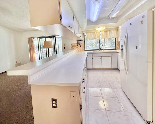 kitchen featuring white refrigerator with ice dispenser, light countertops, a sink, a textured ceiling, and a peninsula