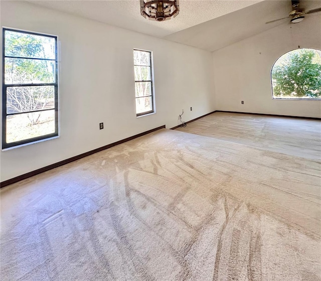 empty room featuring a textured ceiling, light carpet, lofted ceiling, and baseboards