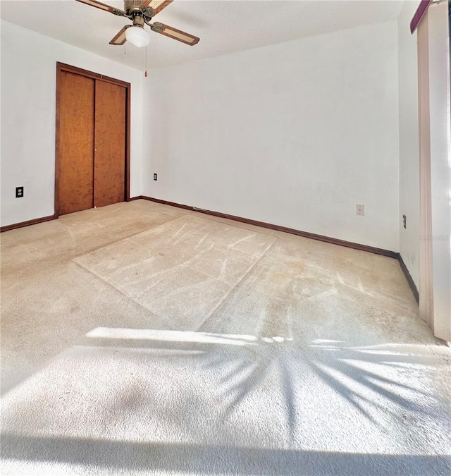 unfurnished bedroom featuring a ceiling fan, a closet, light colored carpet, and baseboards