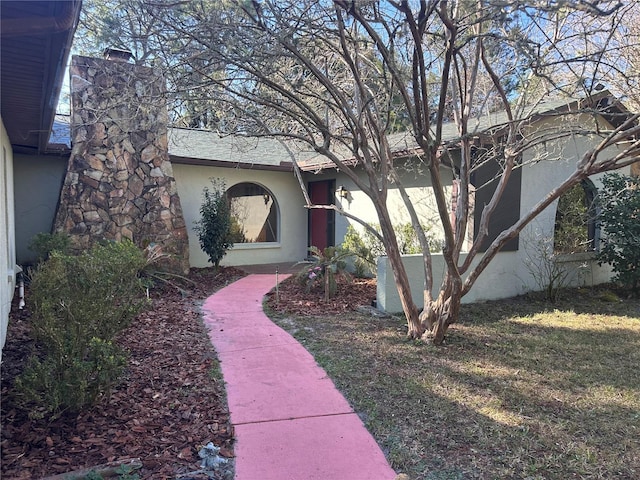 view of exterior entry featuring a shingled roof, a chimney, a lawn, and stucco siding