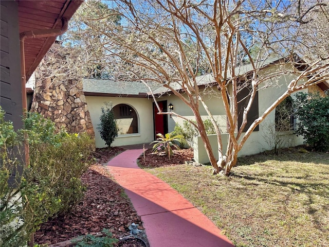 property entrance with a shingled roof, a lawn, and stucco siding