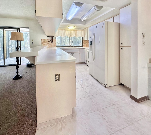 kitchen with light tile patterned floors, a peninsula, white refrigerator with ice dispenser, a sink, and light countertops