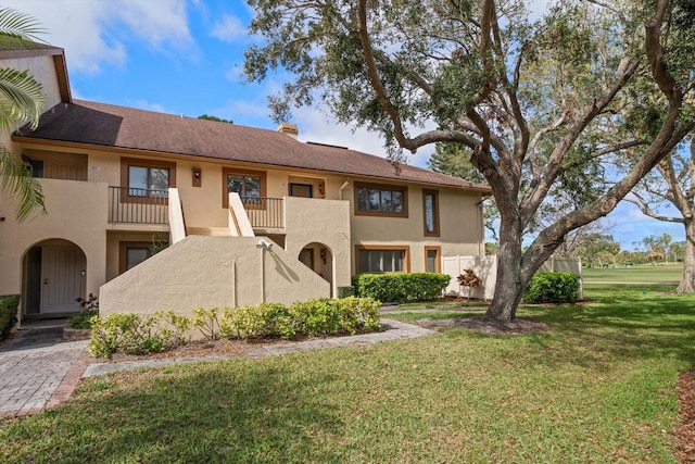 view of front of home with a chimney, a front yard, a balcony, and stucco siding