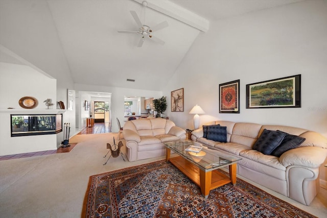 carpeted living area featuring ceiling fan, high vaulted ceiling, beamed ceiling, and a fireplace with flush hearth