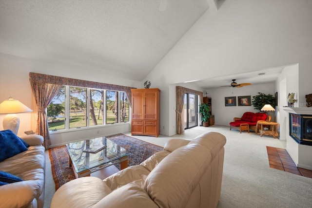 living area with a ceiling fan, a glass covered fireplace, light carpet, a textured ceiling, and high vaulted ceiling