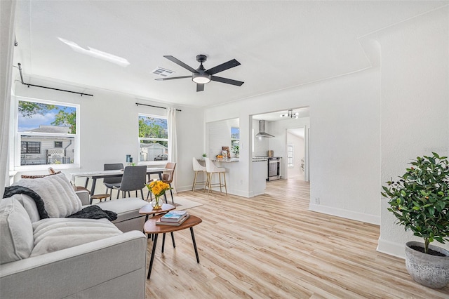 living area with light wood-style floors, ceiling fan, visible vents, and baseboards