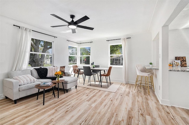 living area featuring ceiling fan, baseboards, and light wood-style floors