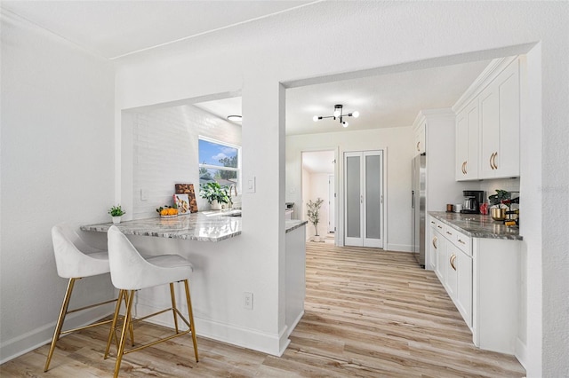 kitchen featuring baseboards, white cabinets, a peninsula, light wood-style floors, and a kitchen bar