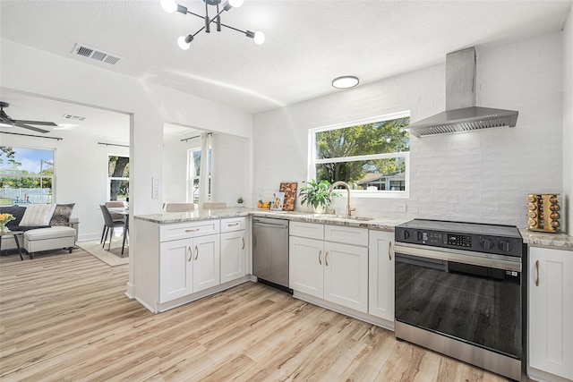 kitchen featuring visible vents, light wood-style floors, electric stove, stainless steel dishwasher, and wall chimney range hood