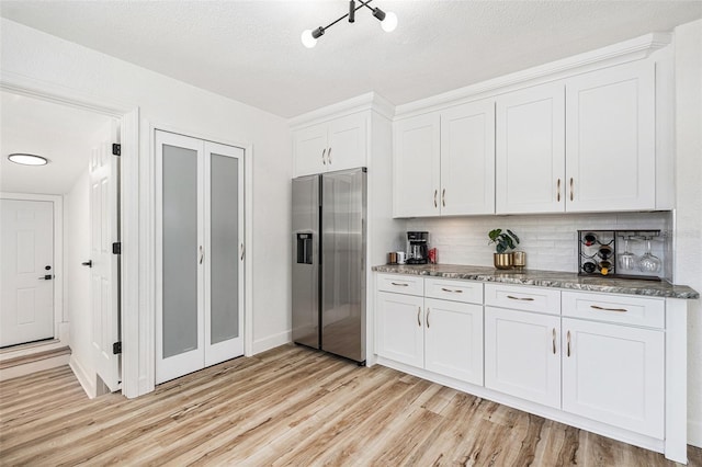 kitchen featuring white cabinets, decorative backsplash, dark stone countertops, light wood-type flooring, and stainless steel refrigerator with ice dispenser