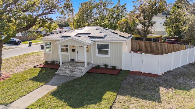 view of front of property featuring roof with shingles, a front yard, fence, and roof mounted solar panels