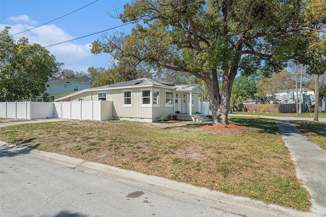 bungalow-style home with a front yard, roof mounted solar panels, and fence