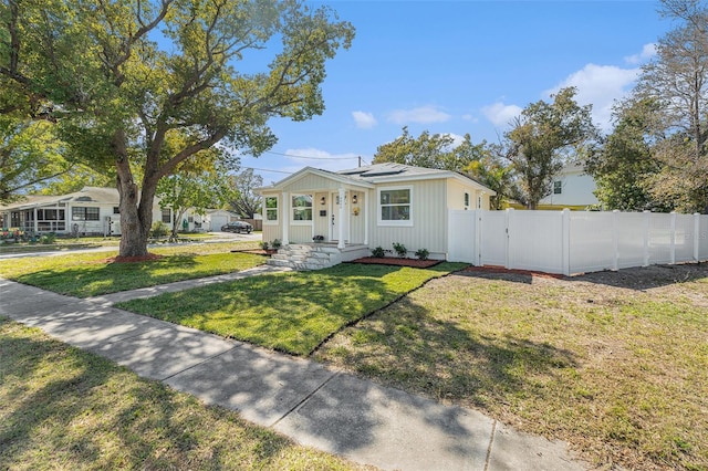 bungalow featuring a front yard, a gate, fence, and roof mounted solar panels