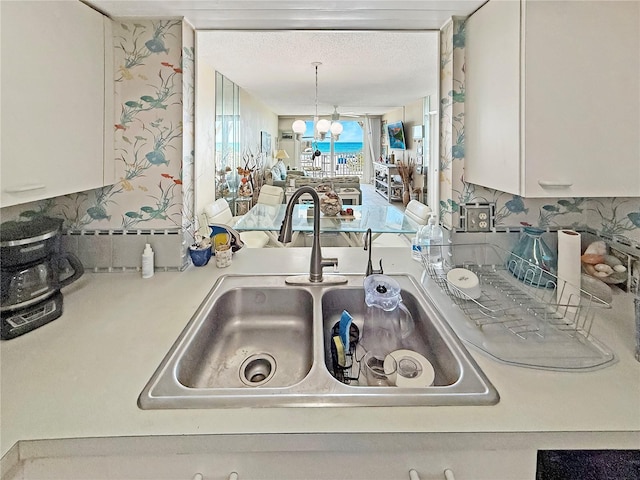 kitchen with tasteful backsplash, light countertops, an inviting chandelier, white cabinets, and a sink