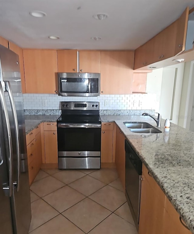 kitchen with light tile patterned floors, light stone counters, stainless steel appliances, a sink, and light brown cabinetry