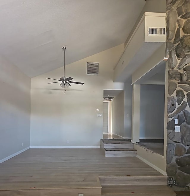 interior space with baseboards, visible vents, a ceiling fan, wood finished floors, and high vaulted ceiling