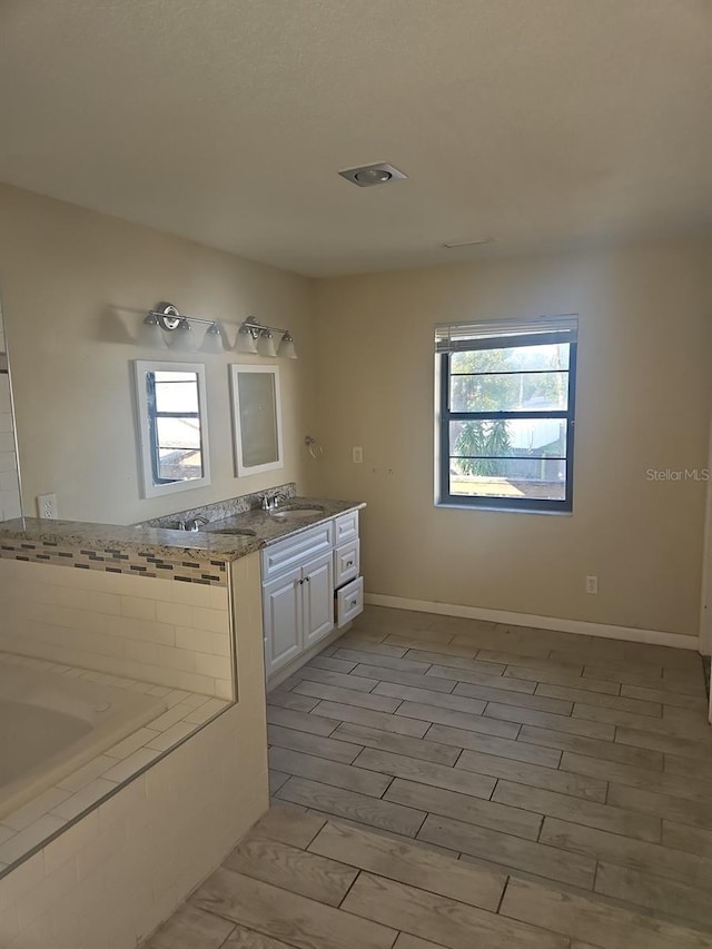 full bathroom with a relaxing tiled tub, a healthy amount of sunlight, vanity, and wood finished floors