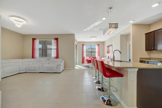 kitchen with baseboards, open floor plan, a kitchen bar, light stone counters, and a sink