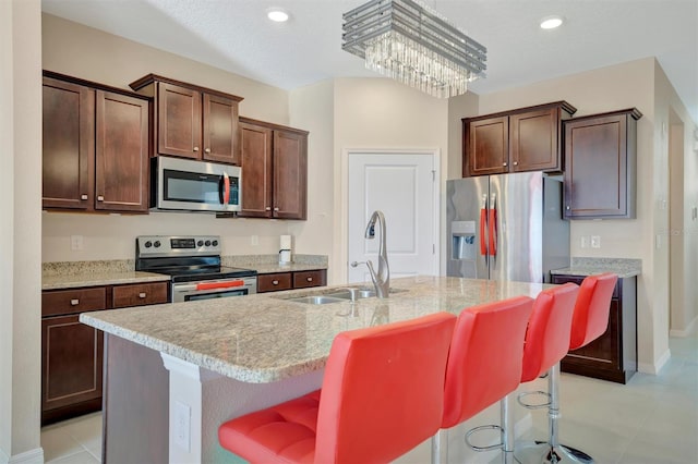 kitchen with a sink, a kitchen breakfast bar, light stone counters, and stainless steel appliances