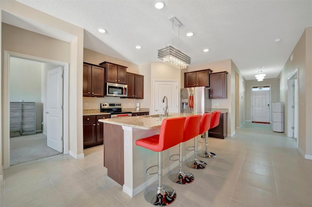 kitchen featuring light tile patterned floors, a kitchen island with sink, a sink, appliances with stainless steel finishes, and a kitchen breakfast bar