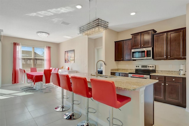 kitchen with a sink, a breakfast bar area, dark brown cabinets, and stainless steel appliances