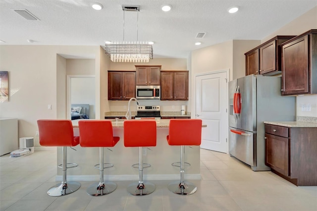 kitchen featuring a kitchen island with sink, a kitchen breakfast bar, visible vents, and appliances with stainless steel finishes